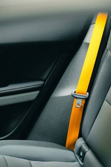 Amber-coloured seat belt webbing running down the interior side panel of a car with the tongue plate resting against the trim.