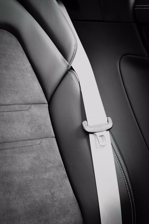 Light grey seat belt webbing crossing a dark car seat, with the tongue plate seated in its guide loop.