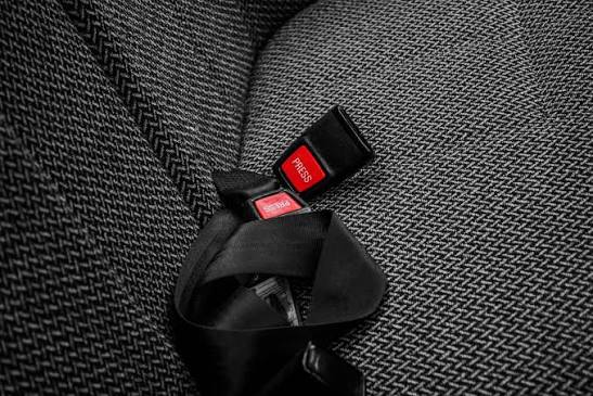 Black seat belt buckle receiver with a red press-release button set into grey herringbone upholstery.