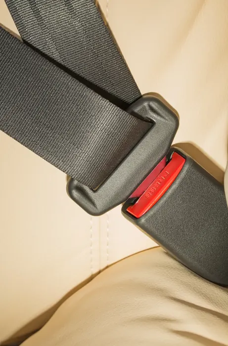 Seat belt tongue plate positioned next to its black buckle receiver with a red release button, against a cream leather vehicle seat.